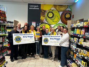 Eine Gruppe von Personen steht bei der Spendenübergabe in einem Supermarkt vor der Leergutannahme. Im Vordergrund werden zwei große Spendenschecks des Lions Clubs „Emy Rogge“ über 840 Euro und 1.260 Euro präsentiert.